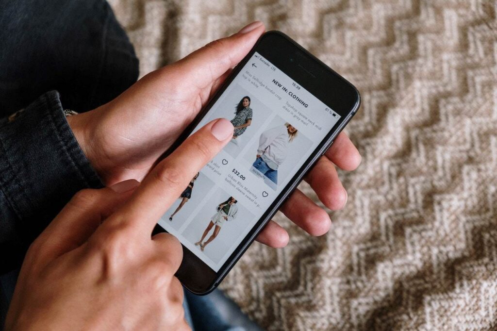 Uma pessoa está com o celular na mão navegando por um site de roupas. A imagem está inserida neste conteúdo para ilustrar que um bom site responsivo melhora a experiência do usuário.