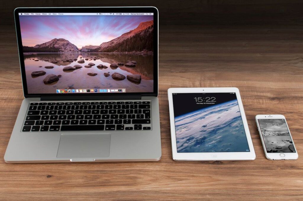 Três aparelhos diferentes em uma mesa: um notebook, um tablet e um celular.