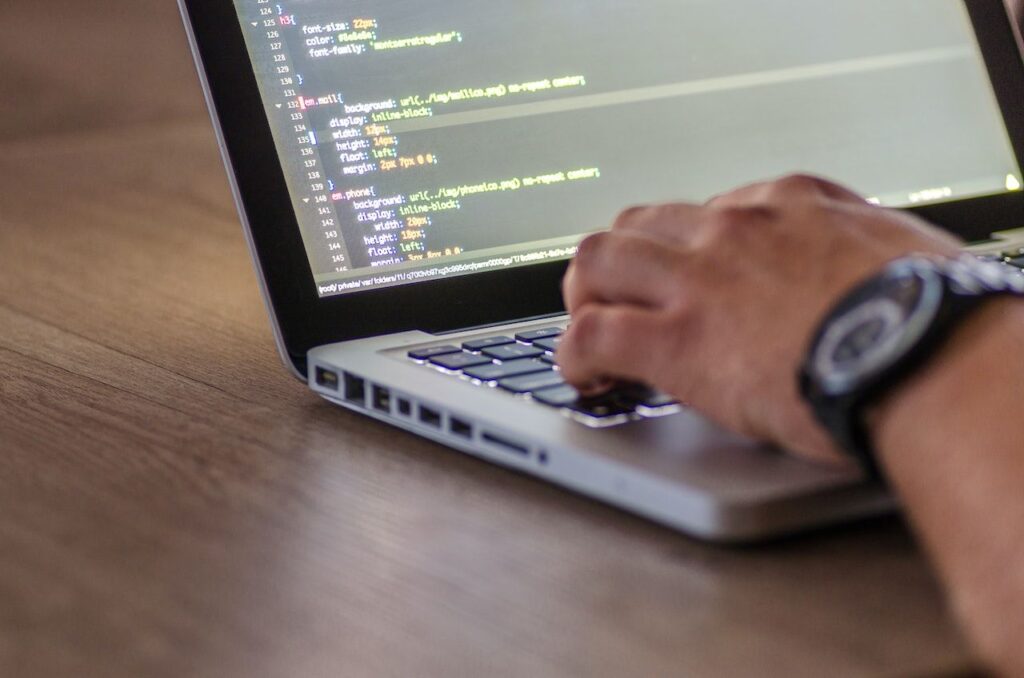Na foto, aparece o braço de uma pessoa mexendo em um computador que apresenta códigos de programação.